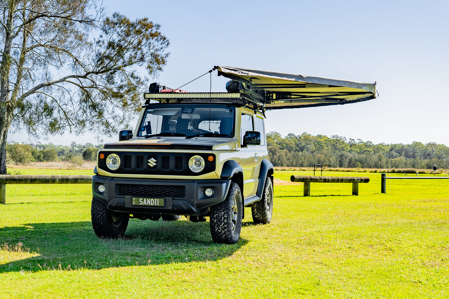 small rooftop tent attached to car parked next to tree in open grass area