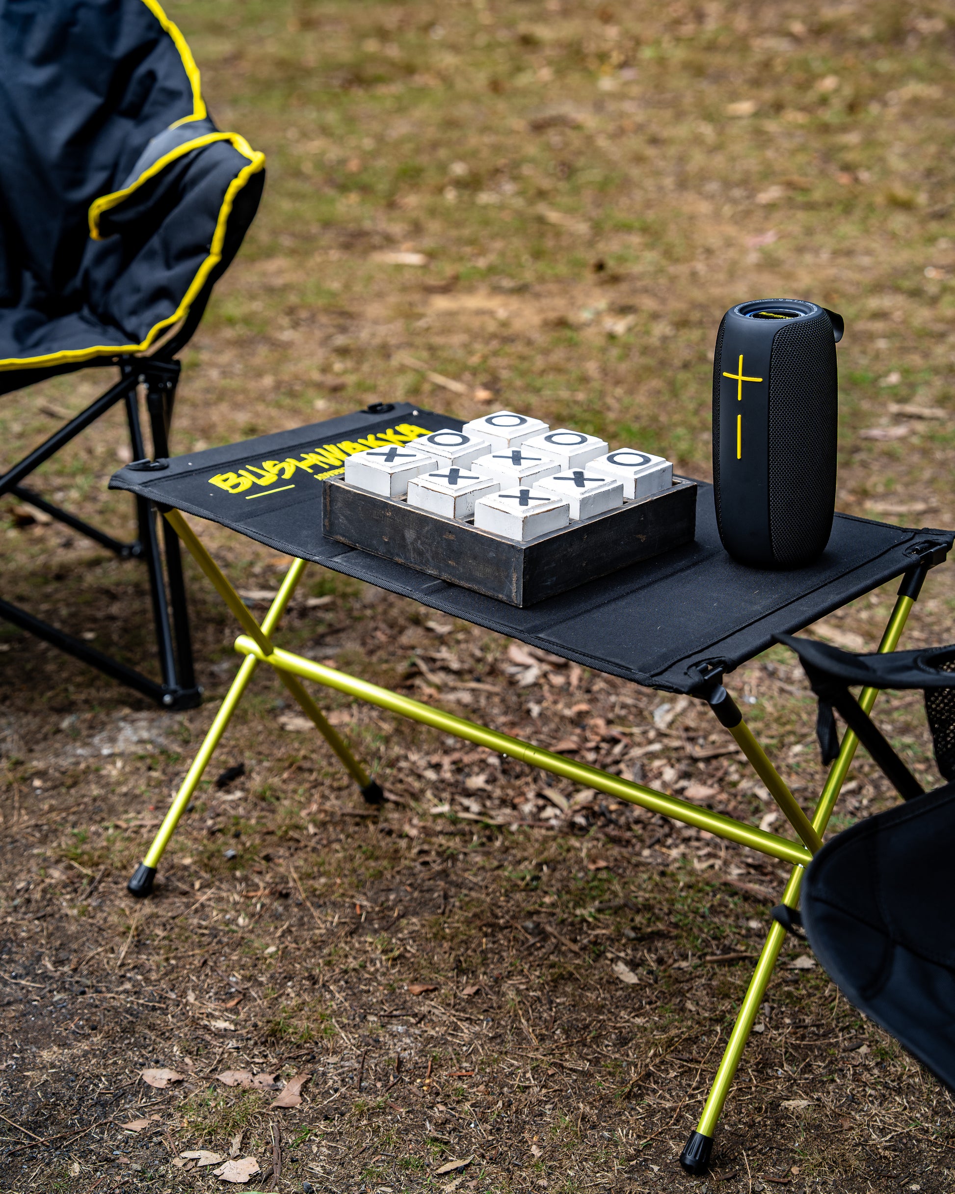 camping table holding a bluetooth speaker and game of naughts and crosses